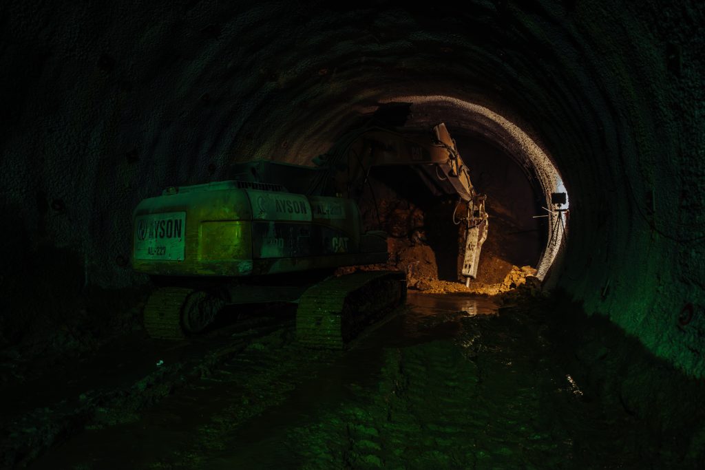 Excavator working inside a tunnel with artificial lighting, showcasing industrial construction and underground infrastructure development.