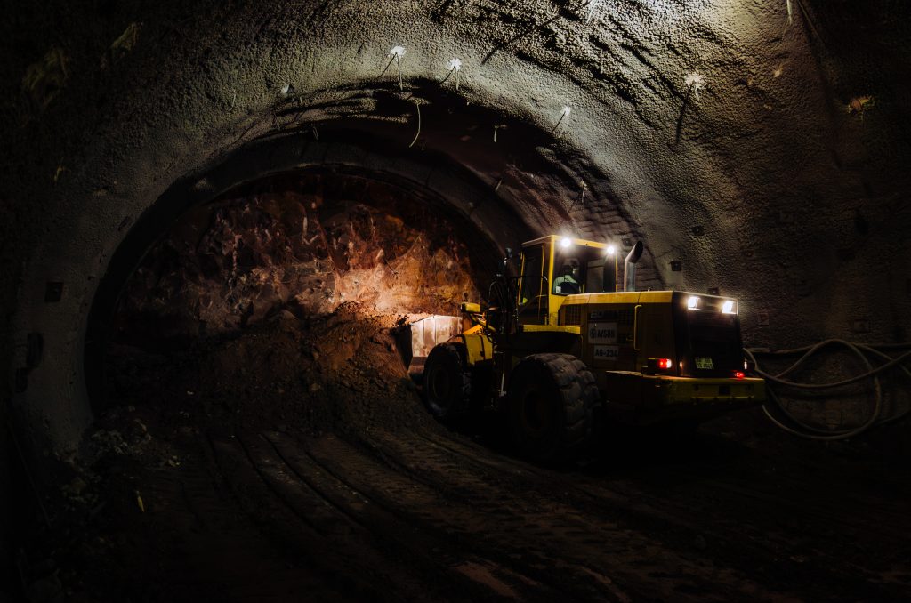 Construction machinery working inside a tunnel at night, illuminated by headlights and interior lights.