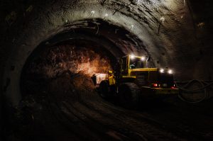 Construction machinery working inside a tunnel at night, illuminated by headlights and interior lights.
