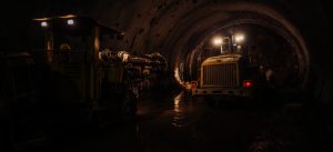 Construction tunnel with heavy machinery and water reflection, illuminated by bright lights in a dark environment.