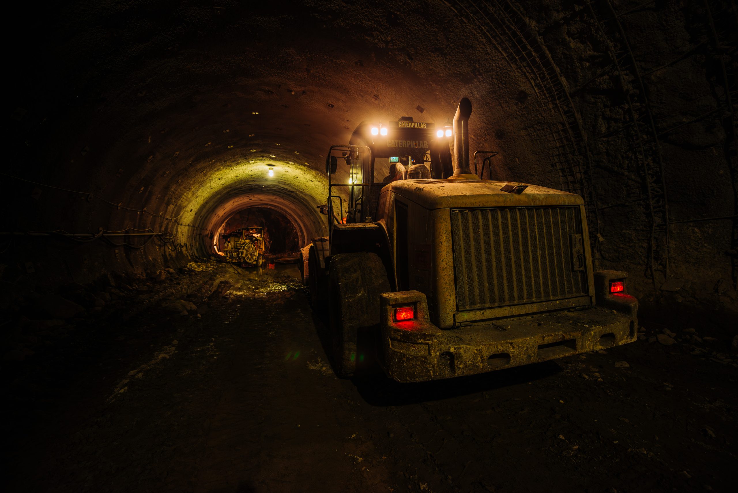 Heavy excavator machinery working inside underground metro tunnel construction site at night with industrial lighting and active civil engineering operations
