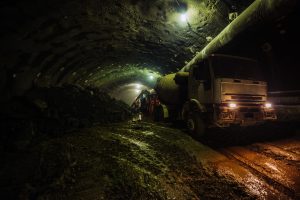 Drilling tunnel construction at night with heavy machinery under artificial lighting in an underground setting.
