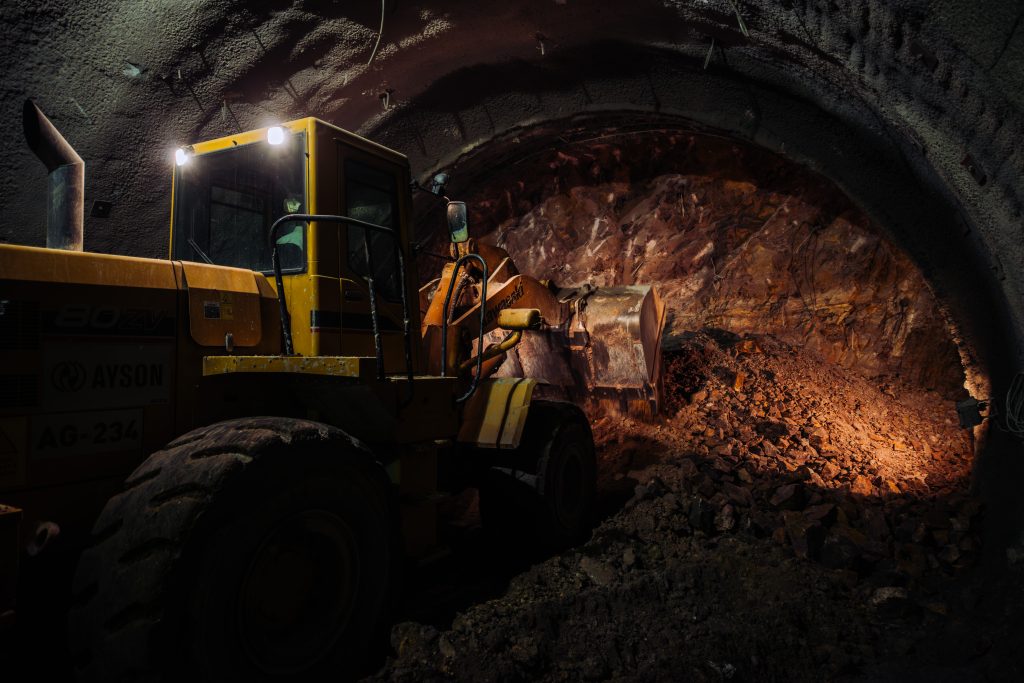 Excavator operating inside tunnel with rocky walls, construction site, industrial machinery, underground engineering, professional photography for industrial projects.
