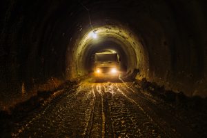 Construction vehicle inside a tunnel with artificial lighting, mud and dirt on the ground, dark, industrial environment.