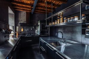 Modern industrial kitchen with black cabinetry, stainless steel countertops, and exposed wooden ceiling in a professional photography portfolio.