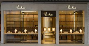 High-end jewelry store window display with mannequins showcasing necklaces and jewelry, modern storefront with elegant lighting, gold accents, and stylish interior design.