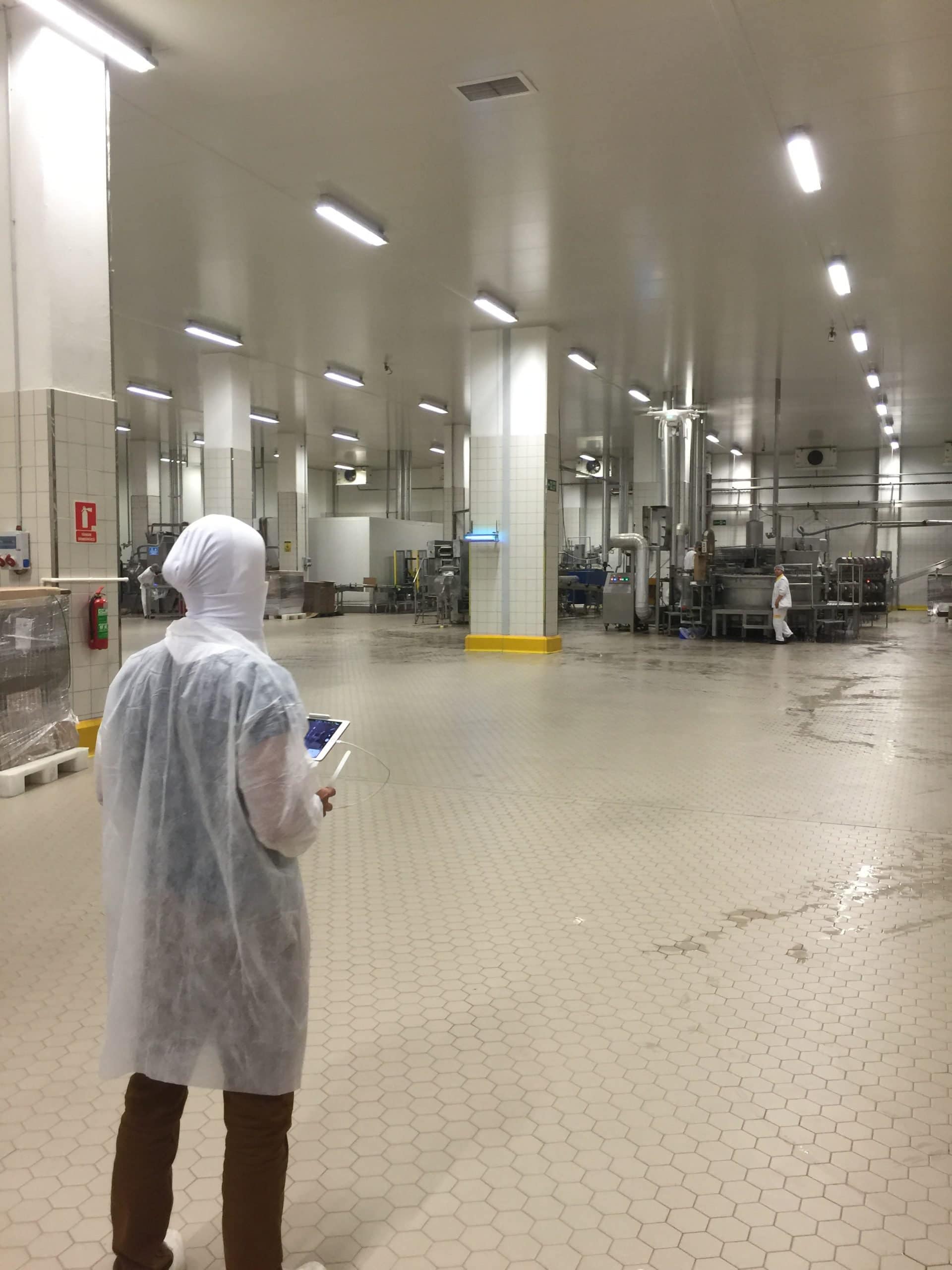 Aerial view of a food production facility with workers in protective clothing inside a well-lit industrial kitchen. The clean, organized space highlights industrial and hospitality photography excellence.