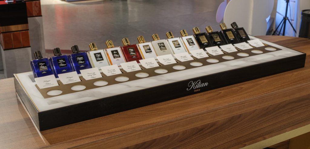 Perfume bottles arranged in a row on a wooden table, showcasing various colors and designs in a retail environment.