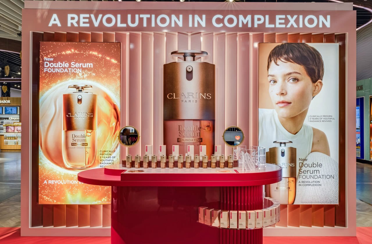 A promotional setup showcasing Clarins Double Serum Foundation with vibrant posters and product arrangement.